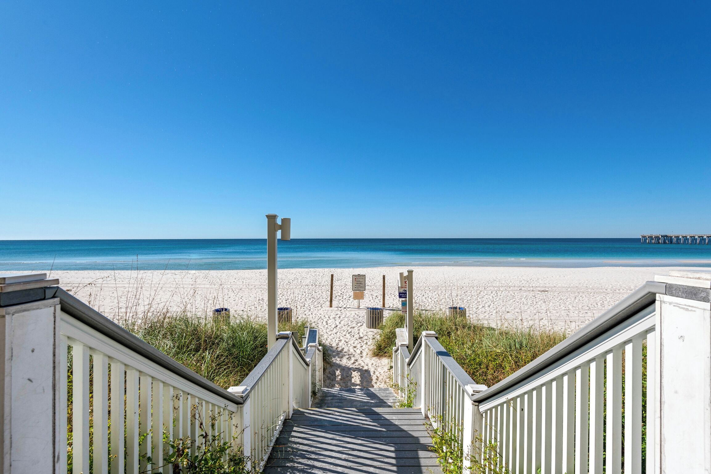 Un escalier en bois menant à une plage, avec un ciel bleu dégagé.