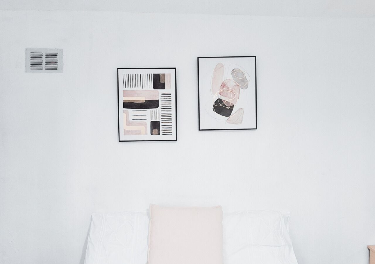 Un dormitorio con una cama, una rejilla de ventilación y dos cuadros en la pared.