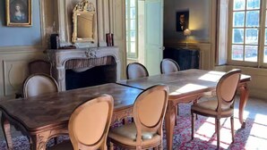 A dining room with a large wooden table and four chairs, a fireplace, and a patterned rug. - Gite des Cerfs (La Ferté-Saint-Aubin)