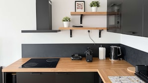 A modern kitchen with a black induction cooktop, a coffee machine, and a kettle on the counter. There are two white potted plants on floating shelves above the counter. - Casa Sabotino, modern, functional, and cozy (Bologna)