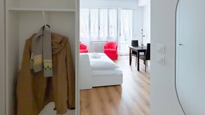 A modern, well-lit room with a white bed, a red chair, and a dining table. - Casa Sabotino, modern, functional, and cozy (Bologna)