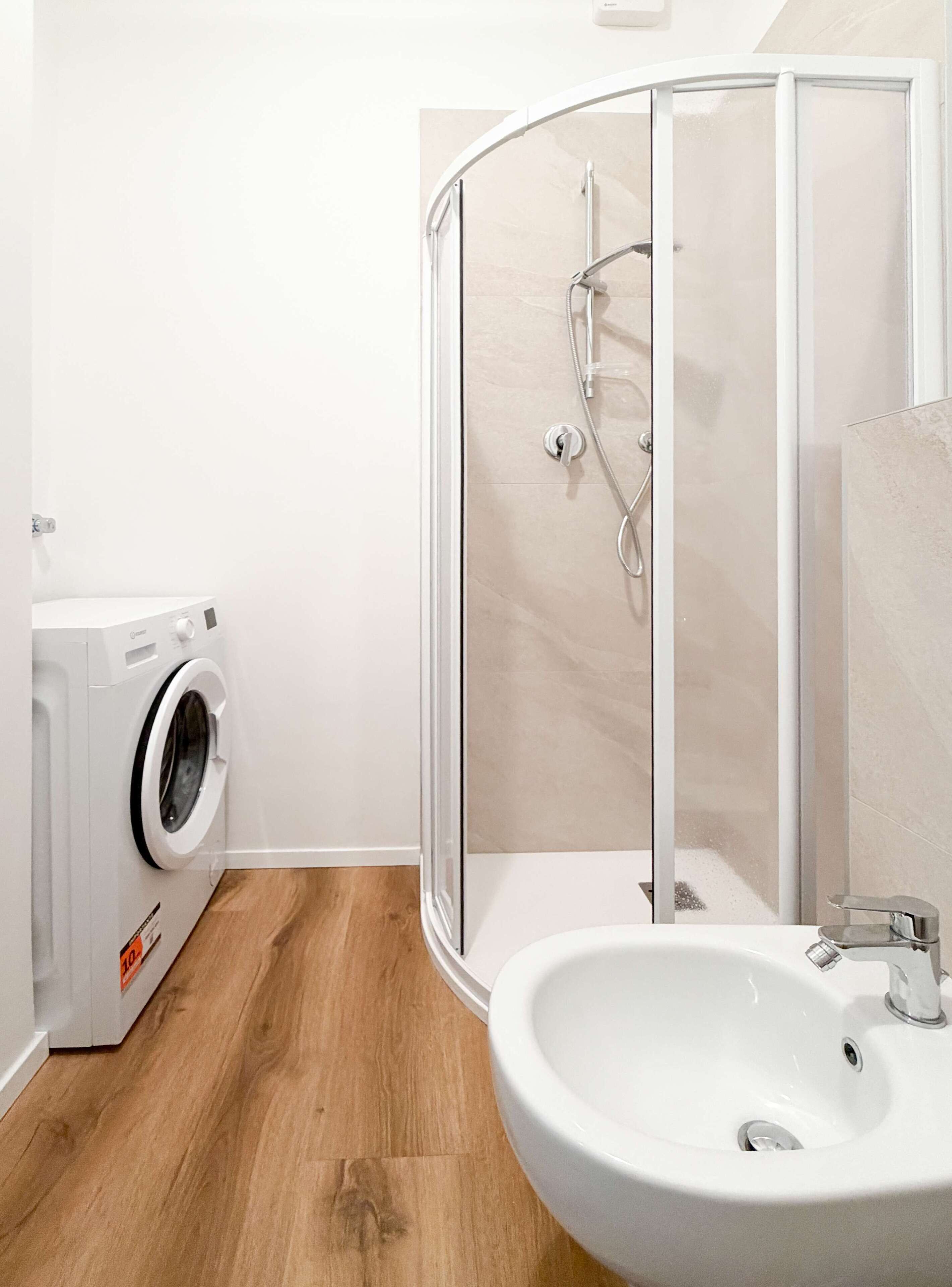 Un bagno moderno con cabina doccia in vetro, lavandino bianco e una lavatrice a carica frontale.