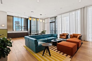 A modern living room with a sectional sofa, two leather armchairs, a coffee table, and a dining area with a view of the city skyline. - 1BR in Miami Worldcenter | Pool + Brightline (Miami)