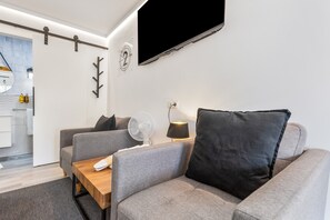 Un salon moderne avec un canapé, une table basse, un téléviseur fixé au mur et un ventilateur.
