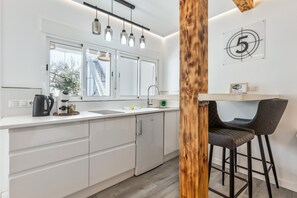 Une cuisine moderne avec des meubles blancs, un four encastré et une machine à café. Un mur d’accent en bois et un panneau portant le chiffre cinq ornent le mur.