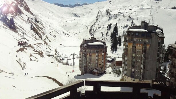 Eine verschneite Berglandschaft mit zwei mehrstöckigen Gebäuden, vermutlich ein Hotel, und einer Seilbahn im Hintergrund.