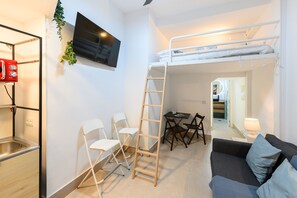 A compact living space with a bunk bed, a TV mounted on the wall, a kitchenette, and a seating area with a couch and chairs. - M Iri70 Acogedor D Plex en el Barrio Salamanca (Madrid)