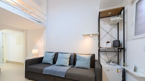 A modern living room with a grey sofa, a small table with a lamp, and a built-in mini-fridge. - M Iri70 Acogedor D Plex en el Barrio Salamanca (Madrid)
