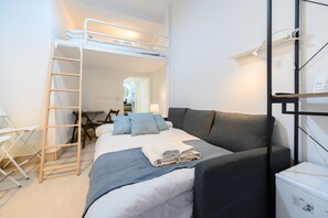 A compact hotel room with a bunk bed, a desk with a chair, a small table, and a refrigerator. - M Iri70 Acogedor D Plex en el Barrio Salamanca (Madrid)