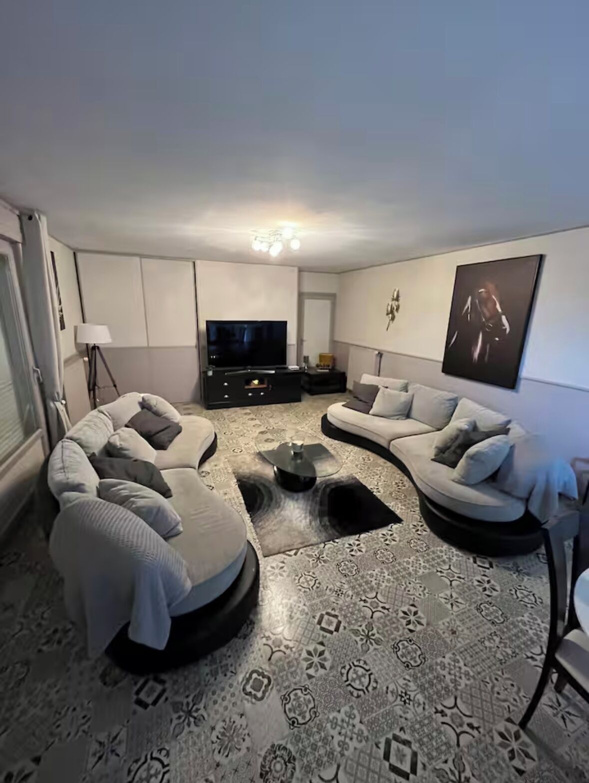A modern living room with a curved sofa set, a flat-screen TV, and patterned flooring.