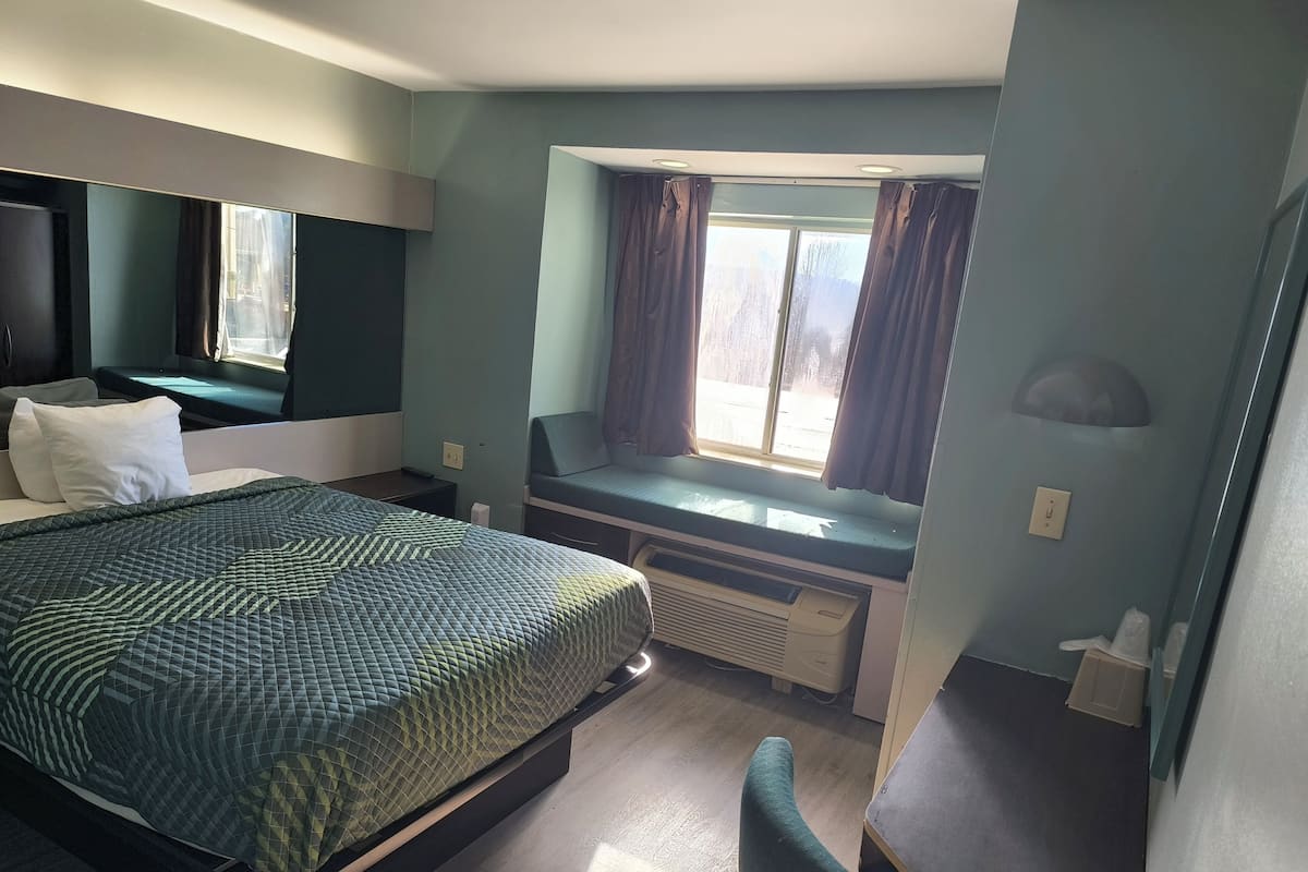 A hotel room with a bed, a desk, and a window with curtains.