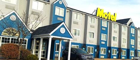 A motel with a blue and white exterior, a covered entrance, and a parking lot.
