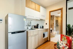 Une cuisine moderne équipée d’un réfrigérateur, d’un four à micro-ondes et d’une machine à café. On trouve un meuble en bois au-dessus de l’évier et une petite fenêtre à l’arrière-plan.