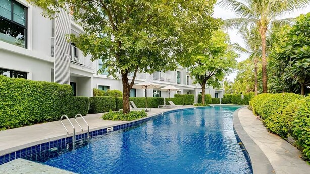 Una piscina con agua cristalina azul, rodeada de setos y árboles bien cuidados.