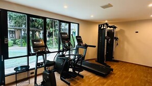 Un gimnasio con cintas de correr, una elíptica y una máquina de pesas, ventanas amplias y piso de madera.