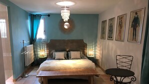 A bedroom with a large bed, a chandelier, a round wall decoration, a radiator, and a small table with a chair. - Room “Apartment, Blue Room” with Shared Pool, Wi-Fi and Air Conditioning (Carpentras)