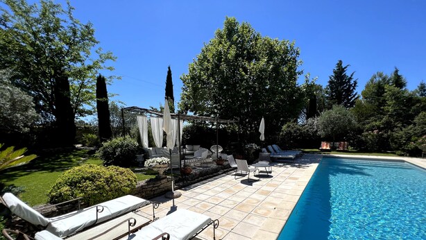 Un espace aménagé au bord de la piscine, avec des chaises longues, une pergola agrémentée de rideaux blancs et une piscine à l’eau d’un bleu limpide.