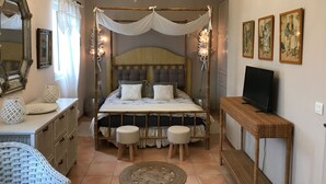 Une chambre à coucher avec un lit à baldaquin, une télévision, un miroir et des œuvres d’art accrochées au mur.