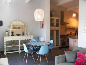 A dining area with a round table, blue chairs, a white cabinet with shelves, and a hanging light fixture.