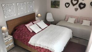 Une chambre à coucher avec un lit en osier, une table de chevet avec une lampe, une chaise, un canapé et des œuvres d’art décoratives accrochées au mur.