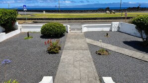 A paved pathway leading to a gated entrance with a view of the sea and mountains. - Pico Island Villas 117 - Natural Pools and Incredible Views (São Roque do Pico)