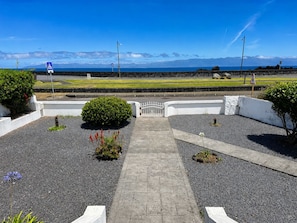 A paved pathway leading to a gated entrance with a view of the sea and mountains. - Pico Island Villas 117 - Natural Pools and Incredible Views (São Roque do Pico)