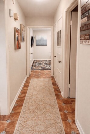Un couloir avec un tapis à motifs, une porte dotée d’une grille d’aération et un mur orné d’œuvres d’art encadrées.