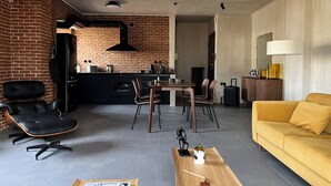 Ein modernes Wohnzimmer mit Essbereich, einem gelben Sofa, einem schwarzen Ledersessel und einer Küche im Hintergrund.