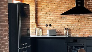Eine Küche mit Backsteinwand, einem schwarzen Kühlschrank, einem Toaster und einem Holztisch.