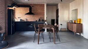 A modern kitchen with a brick wall, a black range hood, and a dining area with a wooden table and chairs. - Wake up in a piece of history (Kavala)