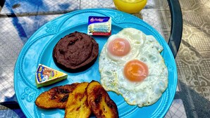 Ein Teller Frühstück mit Eiern, Schokoladenaufstrich, Käsescheibe und gebratenen Kochbananen auf einem blauen Teller.
