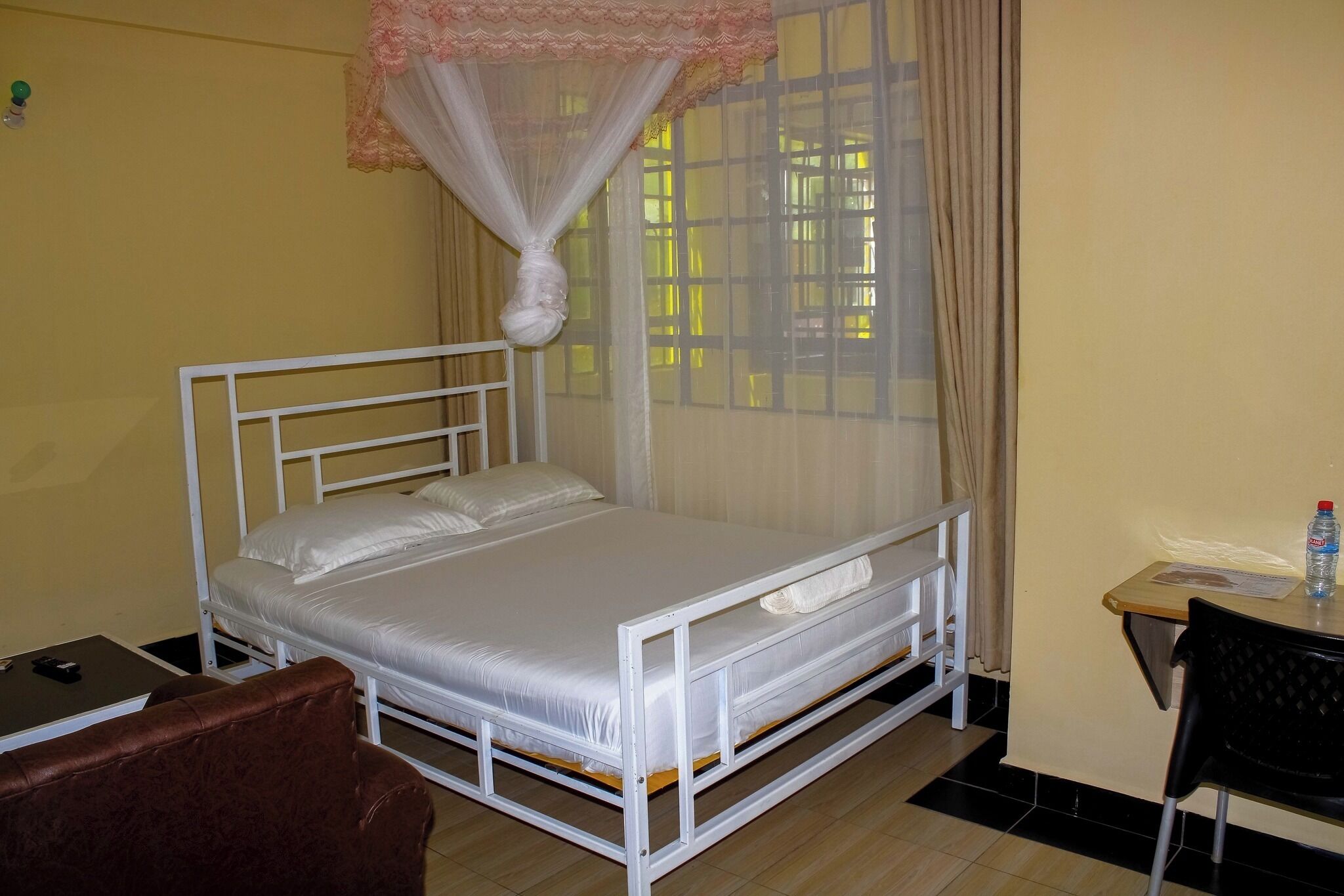 A single-bed room with a mosquito net, a small table with a chair, and a desk with a chair.