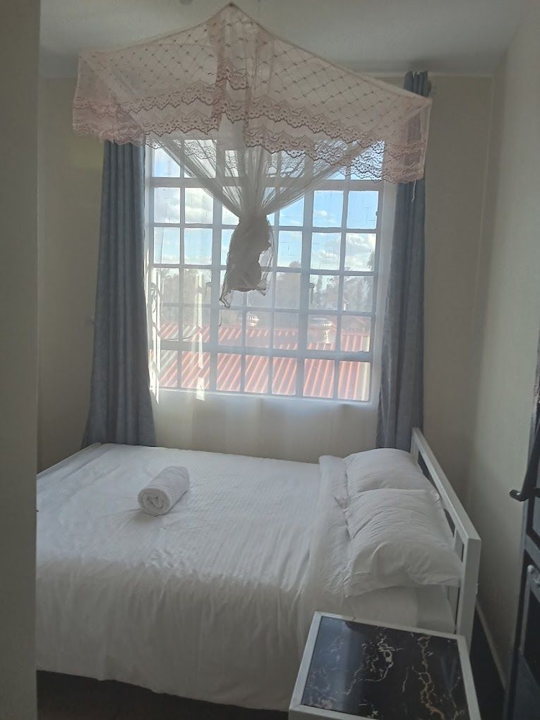 A single bed with a canopy, a bedside table, and a window with curtains.