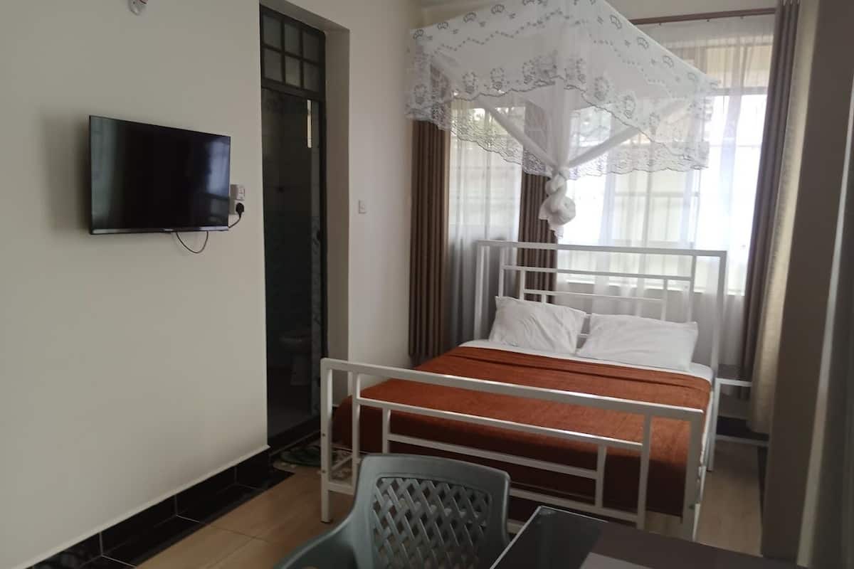 Een hotelkamer met een bed, een aan de muur bevestigde televisie, een tafel met stoel en een raam met gordijnen.