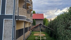 Een meerhoog gebouw met balkons, een structuur met een rood dak op de achtergrond, en een gazon met picknicktafels.