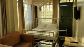 Een eenpersoonskamer met een bed met wit metalen frame, een klein nachtkastje, een stoel en een aan de muur bevestigde televisie.