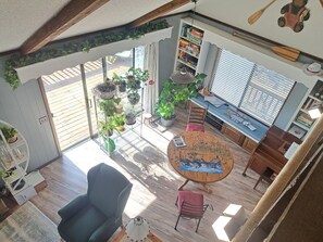 A cozy interior with a wooden floor, a round table with a painting, a blue armchair, and a red chair. There are potted plants, a bookshelf, and a window with blinds. - Bears Den-Secluded cove, Lakefront Cabin, Lake access & Amazing Lake View (Garfield)