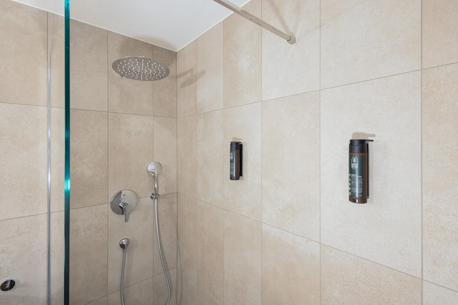 Une salle de bain moderne dotée d’une douche à parois de verre, d’un pommeau de douche à main et de deux robinets muraux.