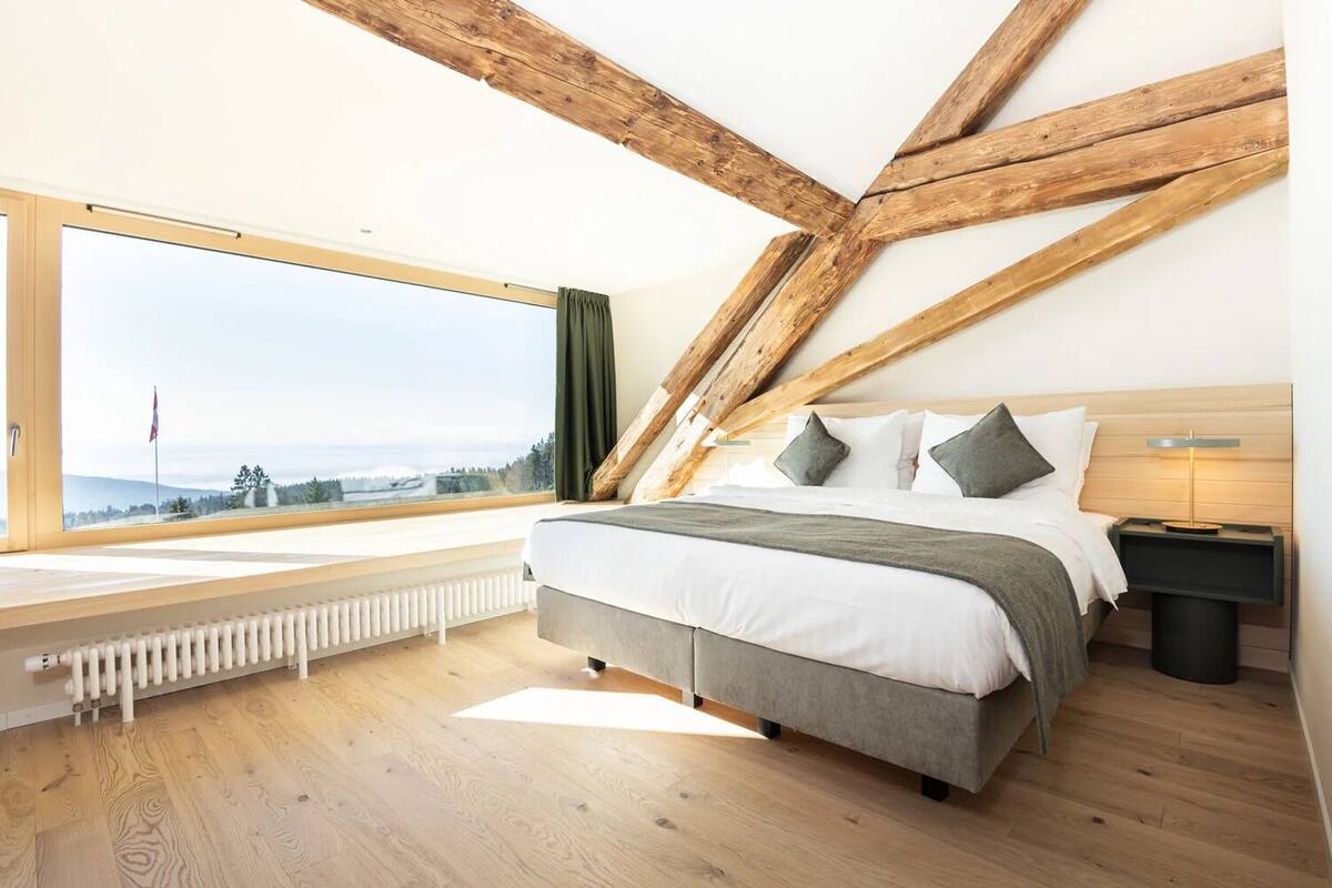 Une chambre avec une grande fenêtre, un lit, une table de chevet et un radiateur.