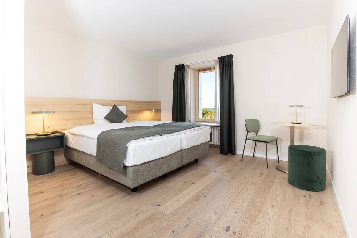 Une chambre d’hôtel moderne équipée d’un lit, d’une table de chevet, d’une chaise et d’une fenêtre avec des rideaux.