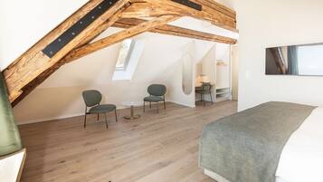 Een slaapkamer in loftstijl met zichtbare houten balken, een bed, twee stoelen, een tafeltje en een spiegel.
