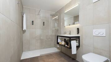 Une salle de bain moderne avec une douche à l’italienne, un meuble-lavabo avec un miroir et des toilettes.