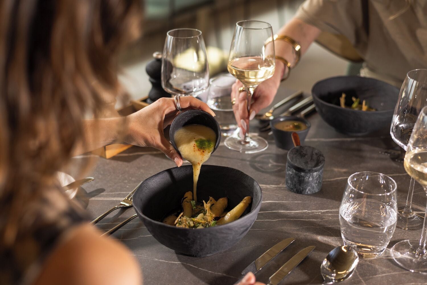 A dining table with bowls, wine glasses, and cutlery.