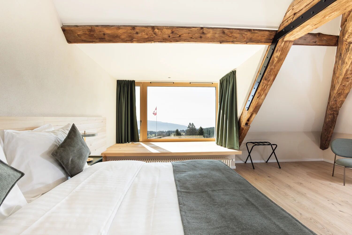 Un dormitorio con cama, ventana con cortinas, vista al exterior y viga de techo de madera.