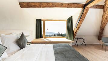 Un dormitorio con cama, ventana con cortinas, vista al exterior y viga de techo de madera.
