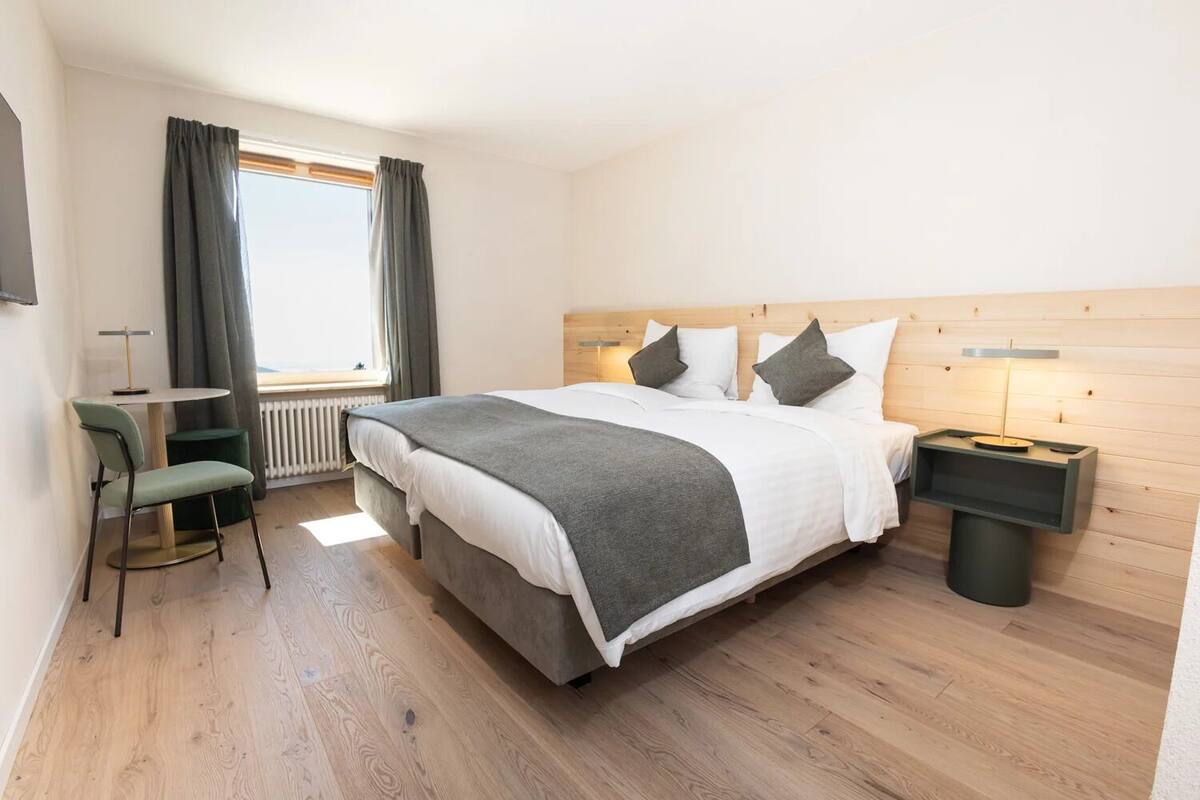 Une chambre d’hôtel moderne avec un grand lit, un petit bureau, une chaise et une table de chevet avec une lampe.