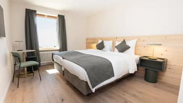 A modern hotel room with a large bed, a small desk, a chair, and a nightstand with a lamp.