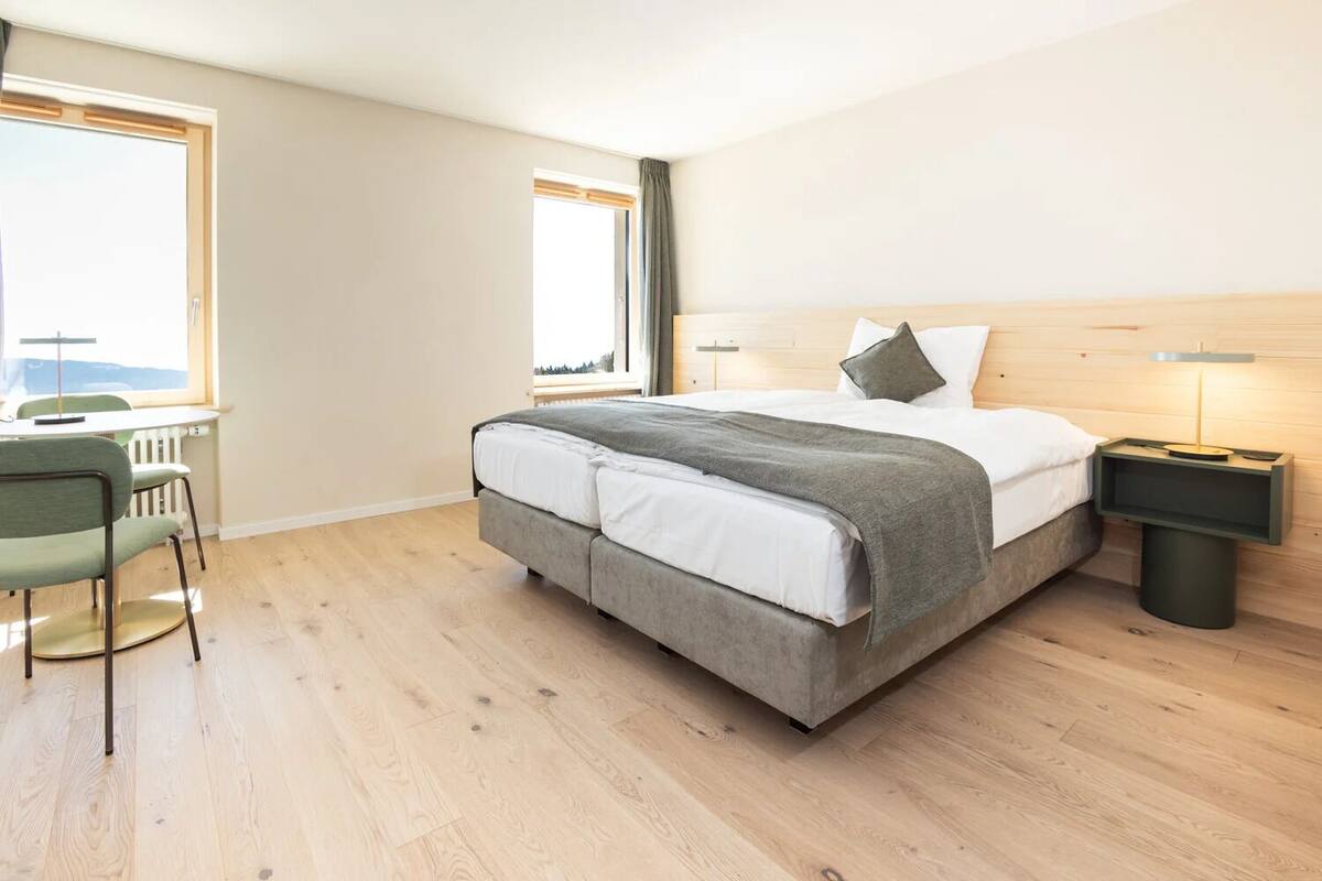 Une chambre à coucher moderne, avec un lit, des tables de chevet, une chaise et de grandes fenêtres.