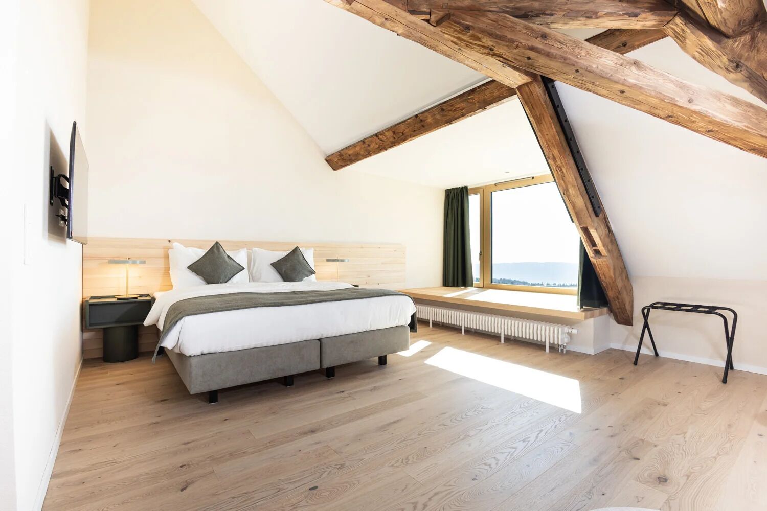 A bedroom with a sloped ceiling, a bed, a nightstand, a window with a view, and a radiator.
