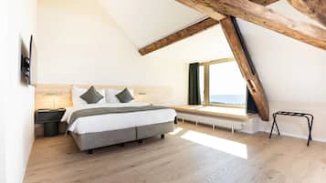 A bedroom with a sloped ceiling, a bed, a nightstand, a window with a view, and a radiator.
